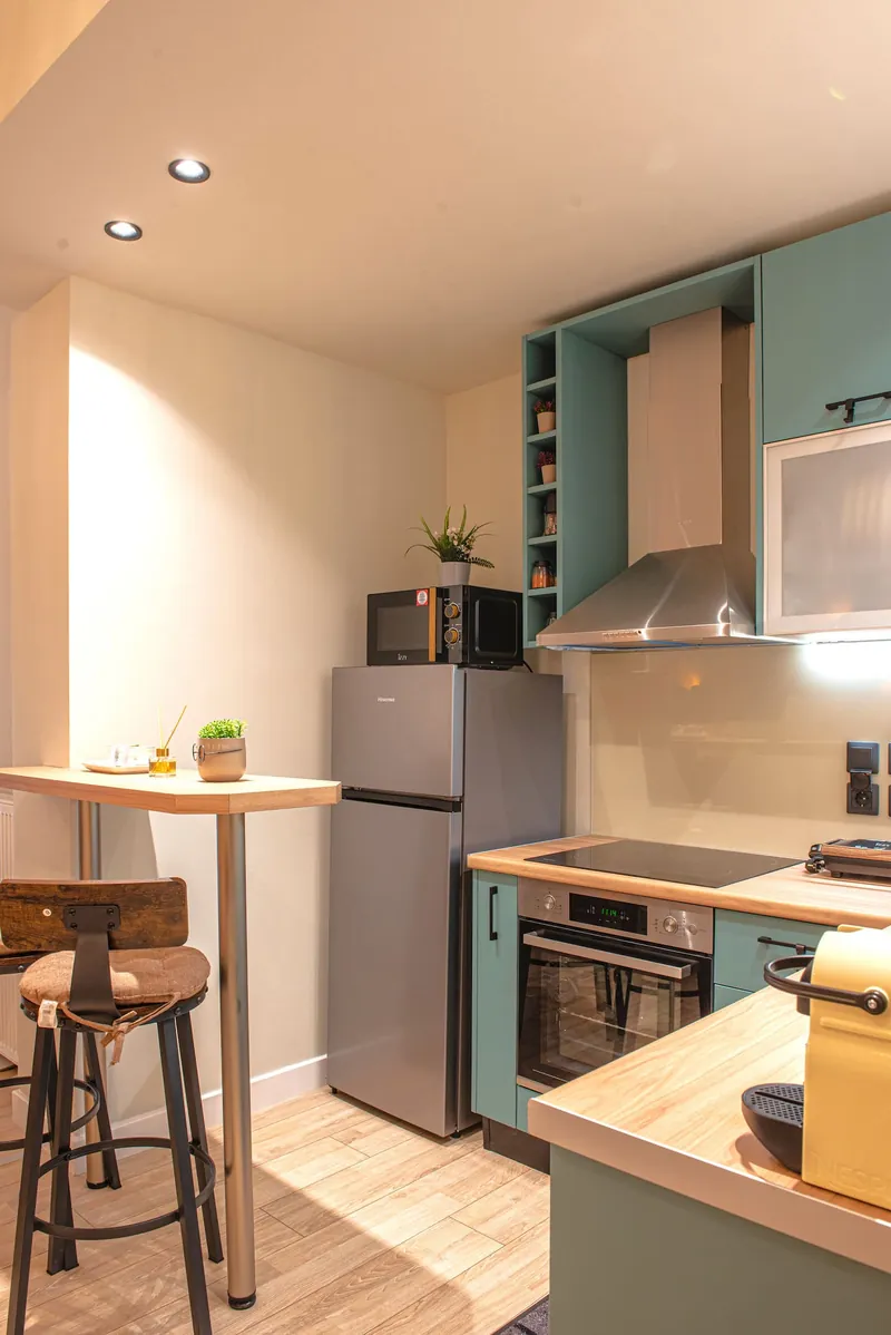 The kitchen with the fridge, the oven and a bar stool