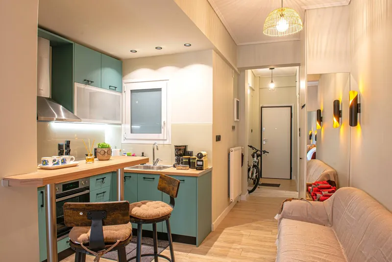 The open-plan room: the teal kitchen, the bar stools and the hallway to the door